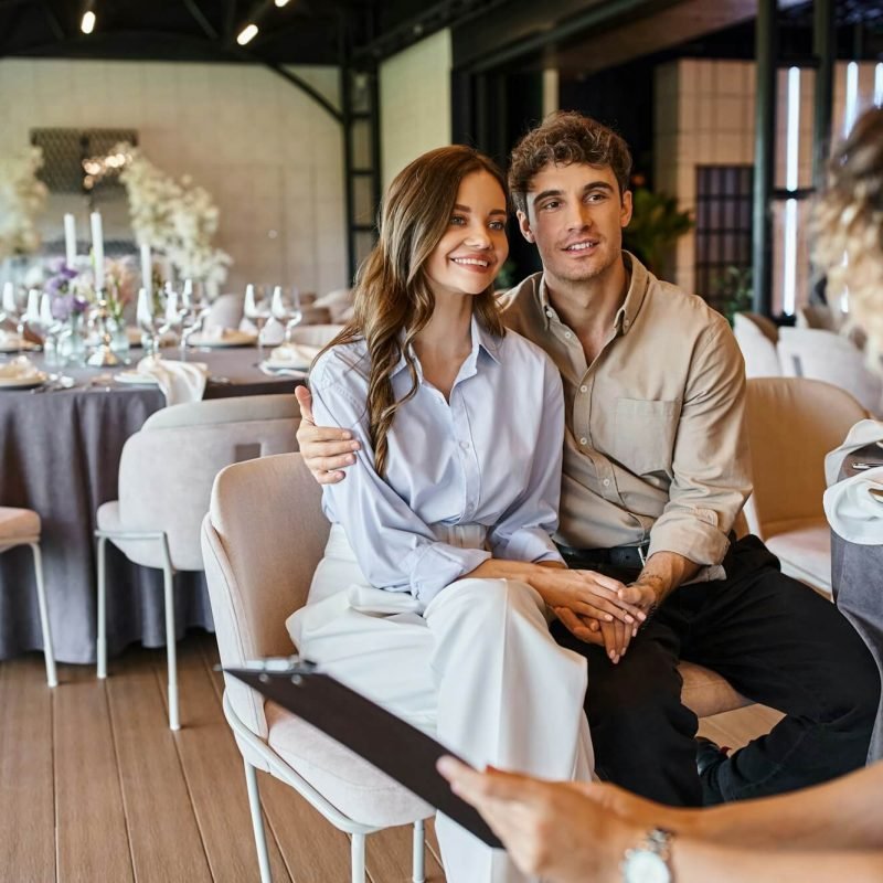 banquet-organizer-with-clipboard-talking-to-couple-in-love-in-event-hall-with-wedding-decor.jpg